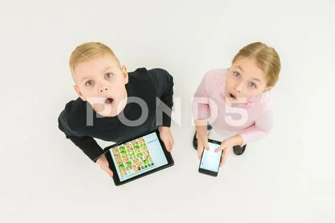 The two surprised kids stand with devices. View from above Stock Photos