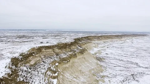 Two SUVs moving along the edge of a sandy cliff of the snow-covered desert in Stock Footage 93836522
