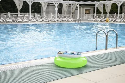 Two swimming circles lie by the pool with blue water on summer day. Stock Photos