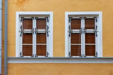 Two symmetrical windows with closed brown wooden shutters and white frames .. Stock Photos