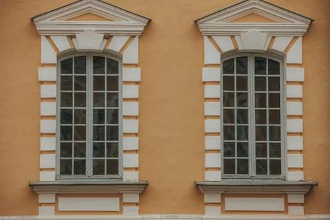 Two symmetrical windows with white frames and decorative molding on an oran.. Stock Photos