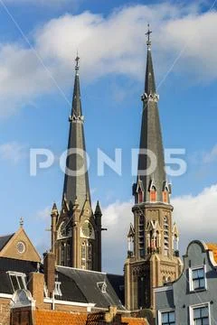 Two tall church spires, one with clock and blue sky and clouds Stock Photos