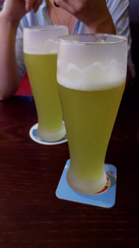 Two tall glasses of pale beer on dark wooden table with blurred pub visitor in 스톡 동영상 345765515
