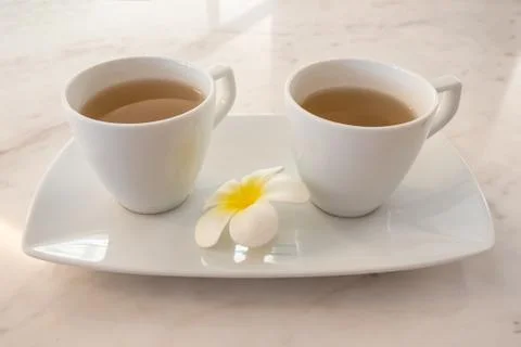Two tea white cup on ceramic tray ready to drink with plumeria flower. Stock Photos