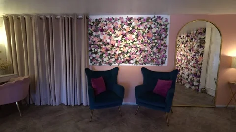 Two teal velvet armchairs below a framed rose panel on a pink wall Stock Footage 345559223