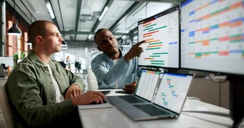 Two Team Members Discuss Project Schedule And Plan Tasks With Laptop Open. Stock Photos