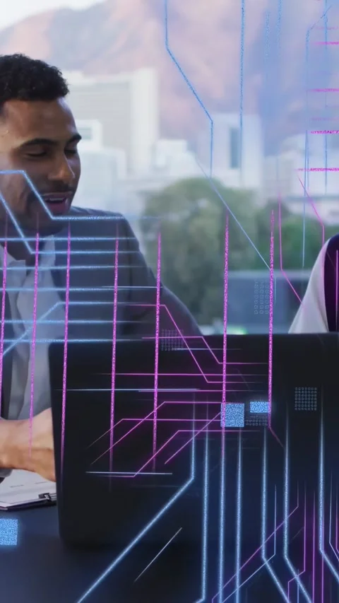 Two tech pros analyzing data at table, laptop sparking neon overlays sweeping Stockbeeldmateriaal 332846552