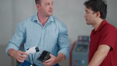 Two technicians show electric vehicle EV charging parts Stockbeeldmateriaal 339546250
