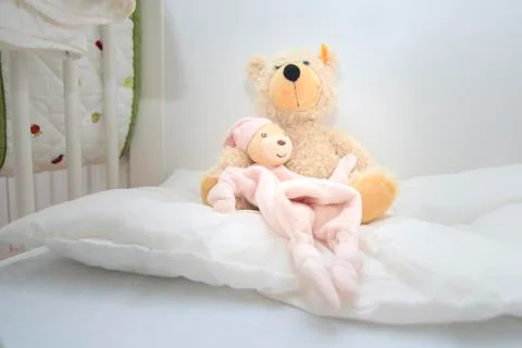 Two teddy bears in baby cott sitting on white pillow Stock Photos