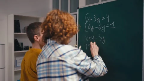 Two teenage boys solving a math problem on chalkboard in class, teamwork Stock Footage 250334135