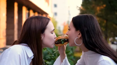 Two teenage friends biting the same hamburger at the same time, two friends Stock Footage 230978109