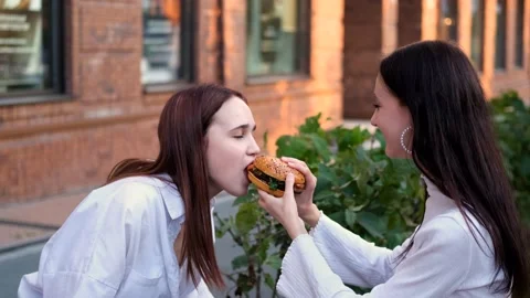 Two teenage friends biting the same hamburger at the same time, two friends Stock Footage 230978261