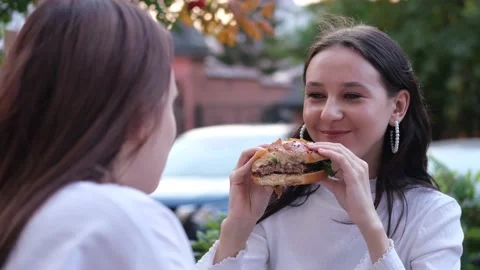 Two teenage friends biting the same hamburger at the same time, two friends Stock Footage 231033367