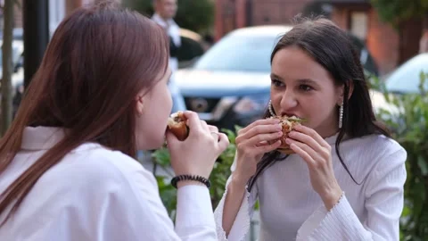 Two teenage friends biting the same hamburger at the same time, two friends Vidéo 231034641