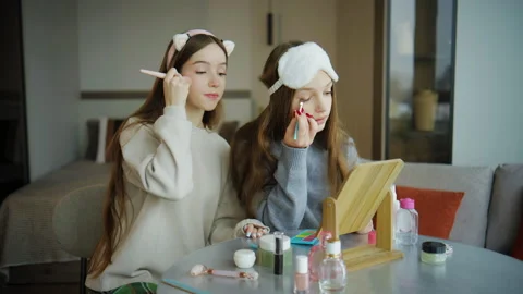 Two teenagers applying makeup in a bright room with a large mirror on a table in Stock Footage 337638040