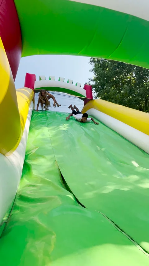 Two teenagers slide down a large inflatable slide at an outdoor event. Joyful Stock Footage 313629654
