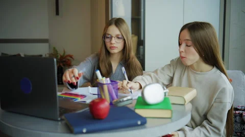 Two teenagers study together at a small round table filled with books and a lapt Stock Footage 337833213