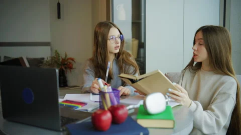 Two teenagers study together at a table with books and a laptop in a modern room Stock Footage 337833208
