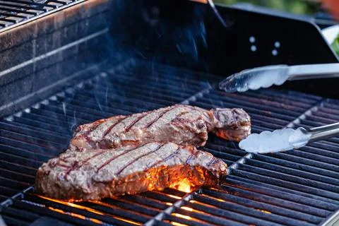 Two thick steaks sizzle over an open flame on a backyard grill Stock Photos