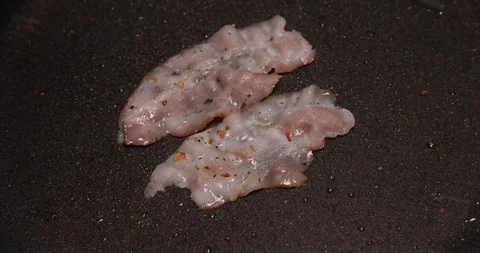 Two thin slices of meat lie in frying pan, frying bacon for breakfast, breakfast Stock Footage 120896378