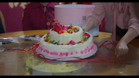 Two-tiered birthday cake on table with hands adjusting ribbon, no face visible Stock Footage 329774363