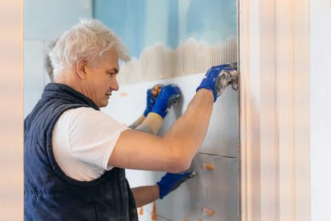 Two tilers installing wall tile at home. Father and son laying tiles on a Stock Photos