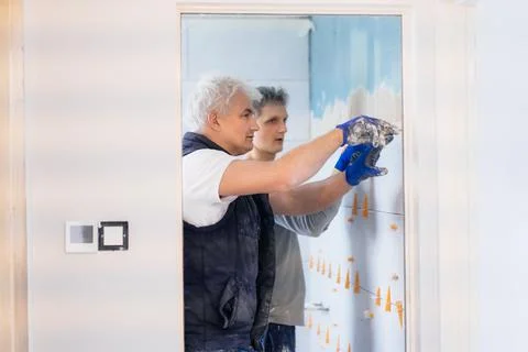 Two tilers installing wall tile at home. Father and son laying tiles on a Stock Photos
