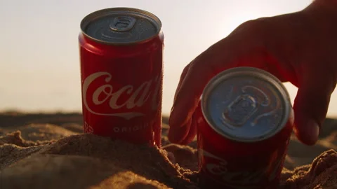 Two tin cans of Coca Cola on a sandy beach with a beautiful sunrise, close-up. Stock Footage 205571854