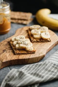 Two toasts with peanut paste, banana slices and chia seeds on a serving woode Stock Photos