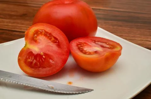 Two tomato halves cut in half in front of a whole tomato on a white plate wit 库存照片