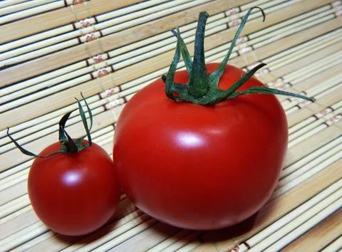 Two tomatoes large and small on a wooden napkin Stock Photos