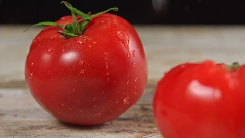 Two tomatoes lie on the Board and the top dripping water in slow motion Video stock 113423627