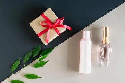 On a two-tone gray-beige background a gift with a red ribbon, a pink cosmetic Stock Photos