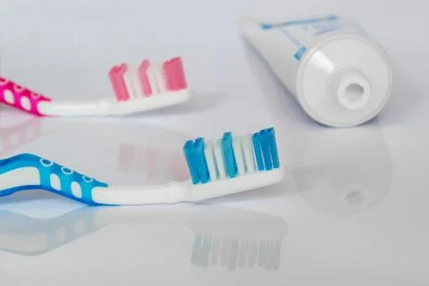 Two toothbrushes and toothpaste on a white glossy background. Stock Photos