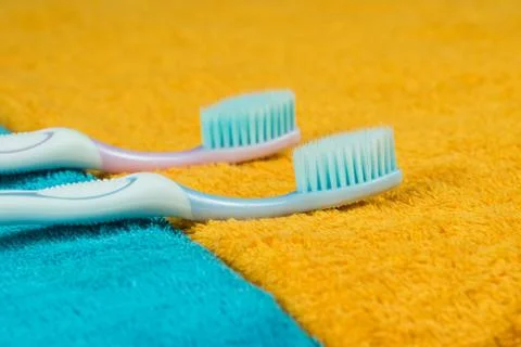 Two toothbrushes lie side by side on yellow and blue towels, side view. Foto stock