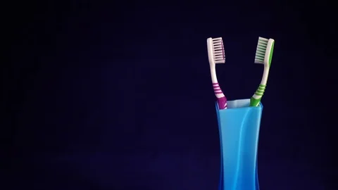 Two toothbrushes, pink and green, stand in a glass or vase on a blue backgrou Stock Footage 87497728