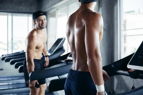 Two topless man exercise walking on treadmill and talking together Stock Photos