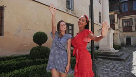 Two tourist friends posing in front of the camera and waving on the city street. Stock Footage 138079533