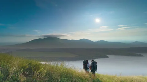 The two tourists standing on mountain top on beautiful river background Stock Footage 159833745