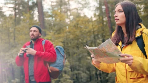 Two tourists stopped in forest glade to check route. Girl examines map while man Stock Footage 147071153