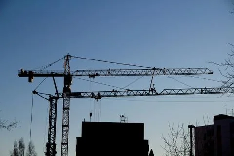 Two tower cranes are working at a construction site against the sky and a hou Stock Photos