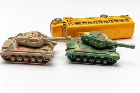 Two toy tanks facing each other beside overturned yellow school bus Fotos de archivo