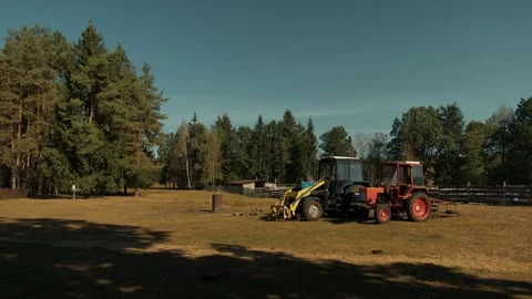 Two tractors parked in clearing next to cattle pen with wooden fence and barn on Stockbeeldmateriaal 317508639