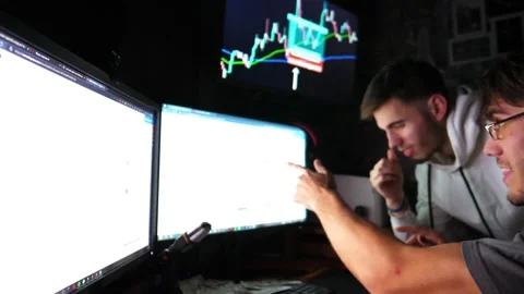 Two traders engaged in cryptocurrency analysis, focused on multiple screens Видео 347870547