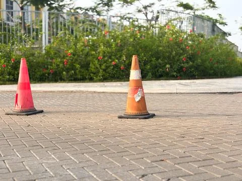 Two traffic cones stand on a brick-paved sidewalk or roadway Stock Photos