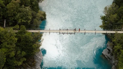 Two trampers walking over bridge crossing a large blue river in New Zealand Vídeos de archivo 89995897