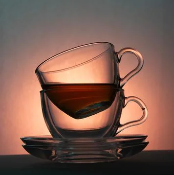 Two transparent cups and two transparent saucers on a light orange background Stock Photos