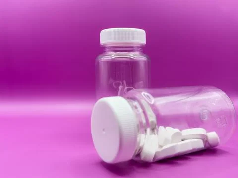 Two transparent jars with white pills, one jar is in the foreground, on a pink Stock Photos