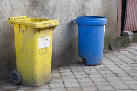 Two trash cans, one yellow and one blue, are sitting on a brick walkway Stock-Fotos