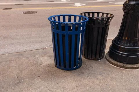 Two trash cans stand on a city street with a light traffic flow during the .. Stock Photos